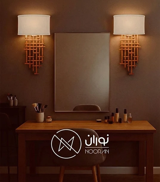چراغ دیواری کلاسیک مدل N2004 با بدنه طلایی بافت‌دار هندسی و شید پارچه‌ای سفید نیم‌دایره، نصب شده در دو طرف آینه میز آرایش در اتاقی با تم قهوه‌ای گرم.