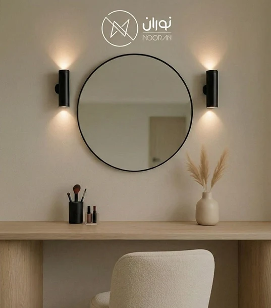 جفت چراغ دیواری مدرن دو طرفه مشکی مدل N1009، نصب شده به صورت متقارن در دو طرف آینه گرد بزرگ بالای میز آرایش با نورپردازی دکوراتیو روی دیوار.