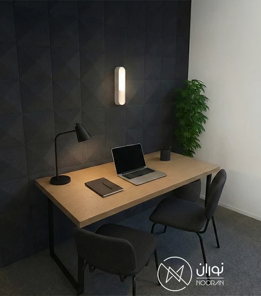 چراغ دیواری مدرن بیضی‌شکل سفید مدل LC140 با نور آفتابی، نصب شده روی دیوار آکوستیک تیره در بالای میز کار چوبی.